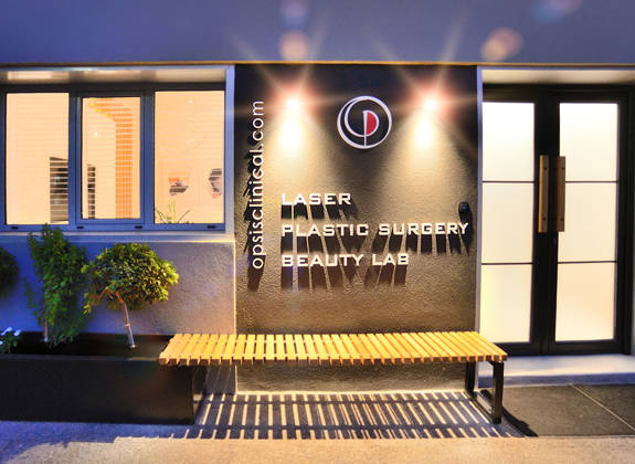 Evening exterior view of Opsis Clinical entrance, featuring laser and plastic surgery beauty lab signage