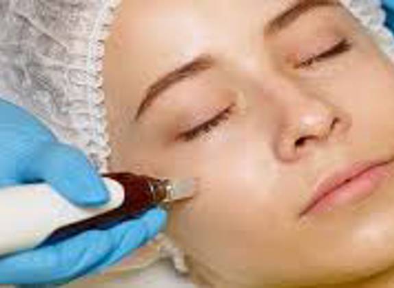 Relaxed woman receiving a microneedling facial treatment with a handheld device applied to her cheek